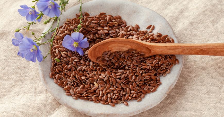 Semi di lino in un piatto con fiori di lino. Ricchi di omega-3, i semi di lino per la colite sono un vero toccasana